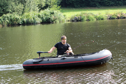Junger Mann im Schlauchboot mit Elektromotor fährt am Fluss.
