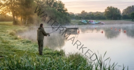 Angler beim Angeln am Badesee im Morgennebel mit Badesteg und Bojen